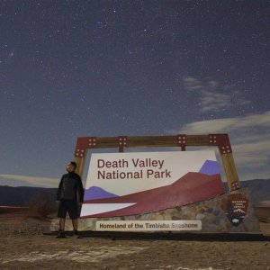 Standing next to the Death Valley sign on starry night with the Andromeda galaxy on left top of the picture. Winter 2013. California, USA.